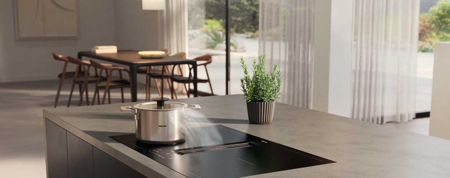 Dampfender Topf steht auf Kochfeld mit integriertem Dunstabzug von Miele in elegantem Wohnraum