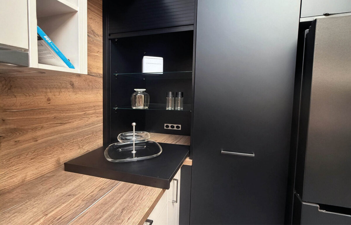 Schwarzer Hochschrank der Häcker Concept Laser Küche mit offener Nische, Glasböden und ausziehbarer Ablage neben der Arbeitsfläche in Holzoptik.