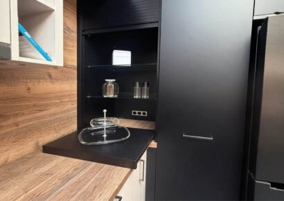 Schwarzer Hochschrank der Häcker Concept Laser Küche mit offener Nische, Glasböden und ausziehbarer Ablage neben der Arbeitsfläche in Holzoptik.