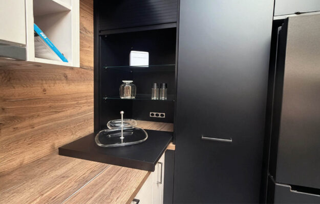 Schwarzer Hochschrank der Häcker Concept Laser Küche mit offener Nische, Glasböden und ausziehbarer Ablage neben der Arbeitsfläche in Holzoptik.