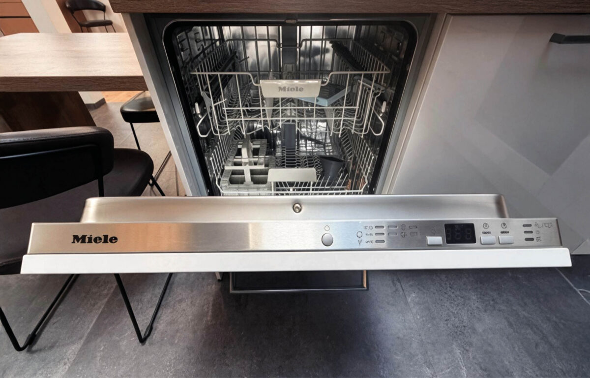 Geöffneter Miele Einbau-Geschirrspüler mit Edelstahl-Bedienleiste und Geschirrkörben in der modernen Häcker Concept Laser Ausstellungsküche.