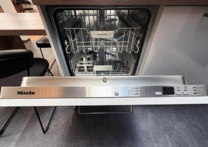Geöffneter Miele Einbau-Geschirrspüler mit Edelstahl-Bedienleiste und Geschirrkörben in der modernen Häcker Concept Laser Ausstellungsküche.