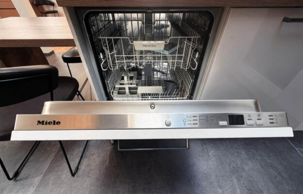 Geöffneter Miele Einbau-Geschirrspüler mit Edelstahl-Bedienleiste und Geschirrkörben in der modernen Häcker Concept Laser Ausstellungsküche.