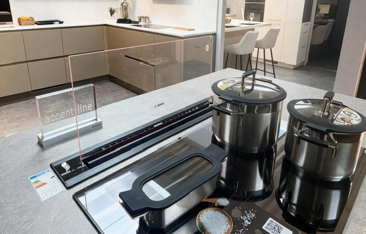 Kochfeld der Nobilia Ausstellungsküche mit berbel Accent Line Tischlüfter, ausfahrbarer Glasblende und Edelstahl-Kochgeschirr auf einer grauen Küchenarbeitsplatte.