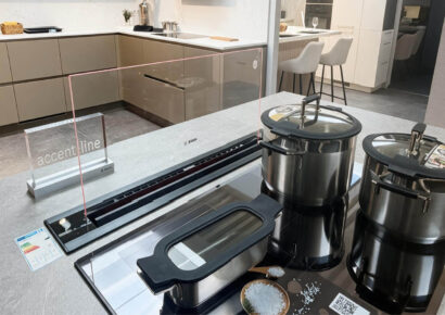 Kochfeld der Nobilia Ausstellungsküche mit berbel Accent Line Tischlüfter, ausfahrbarer Glasblende und Edelstahl-Kochgeschirr auf einer grauen Küchenarbeitsplatte.