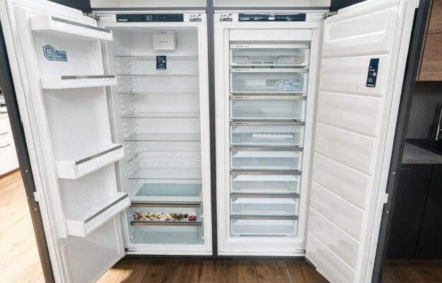 Geöffneter Liebherr Kühlschrank und Gefrierschrank nebeneinander mit Glasablagen, Türfächern, Frischeschublade und mehreren transparenten Gefrierschubladen.